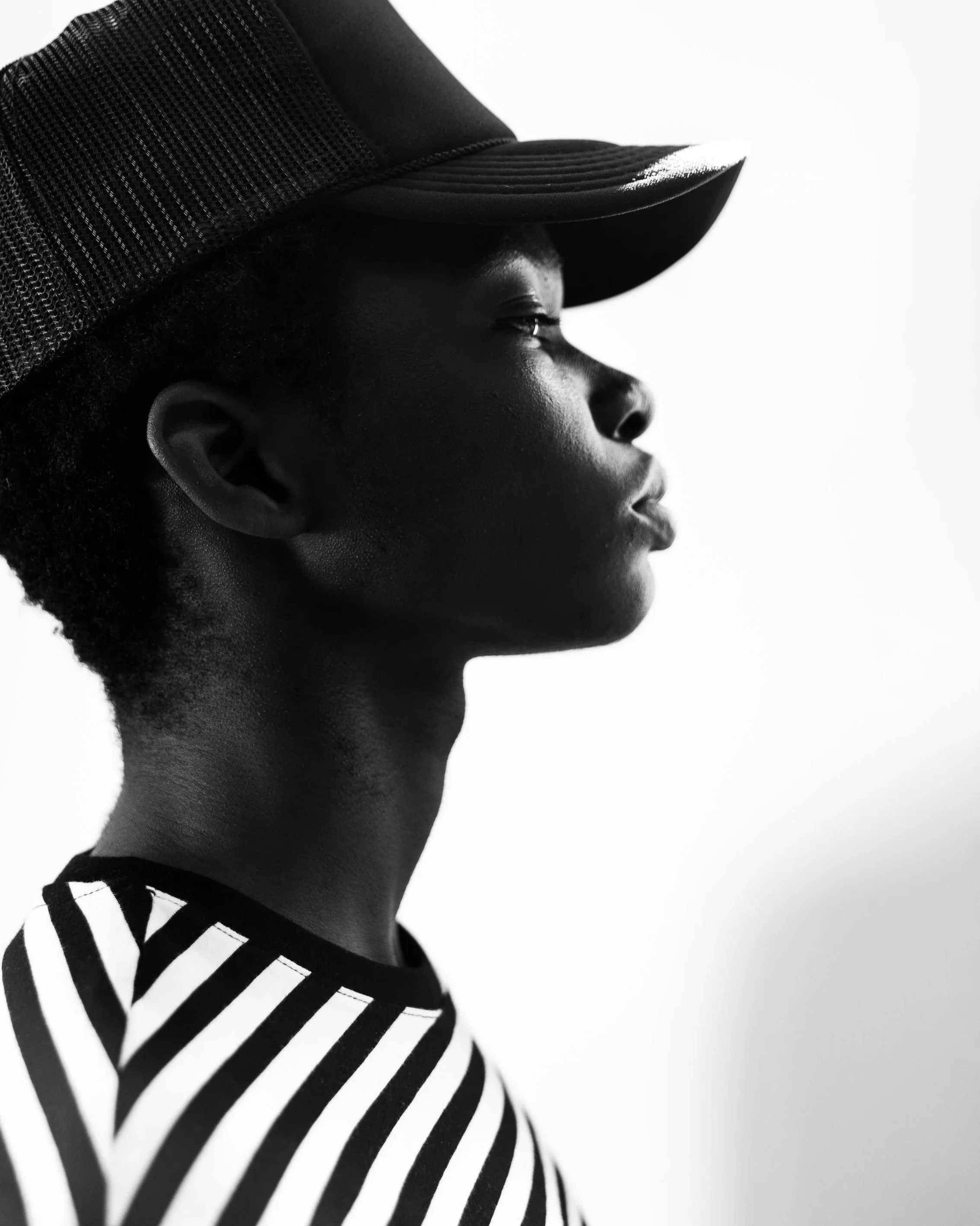 Side profile of a person wearing a black cap and black and white striped shirt, facing to the right, with a plain white background.