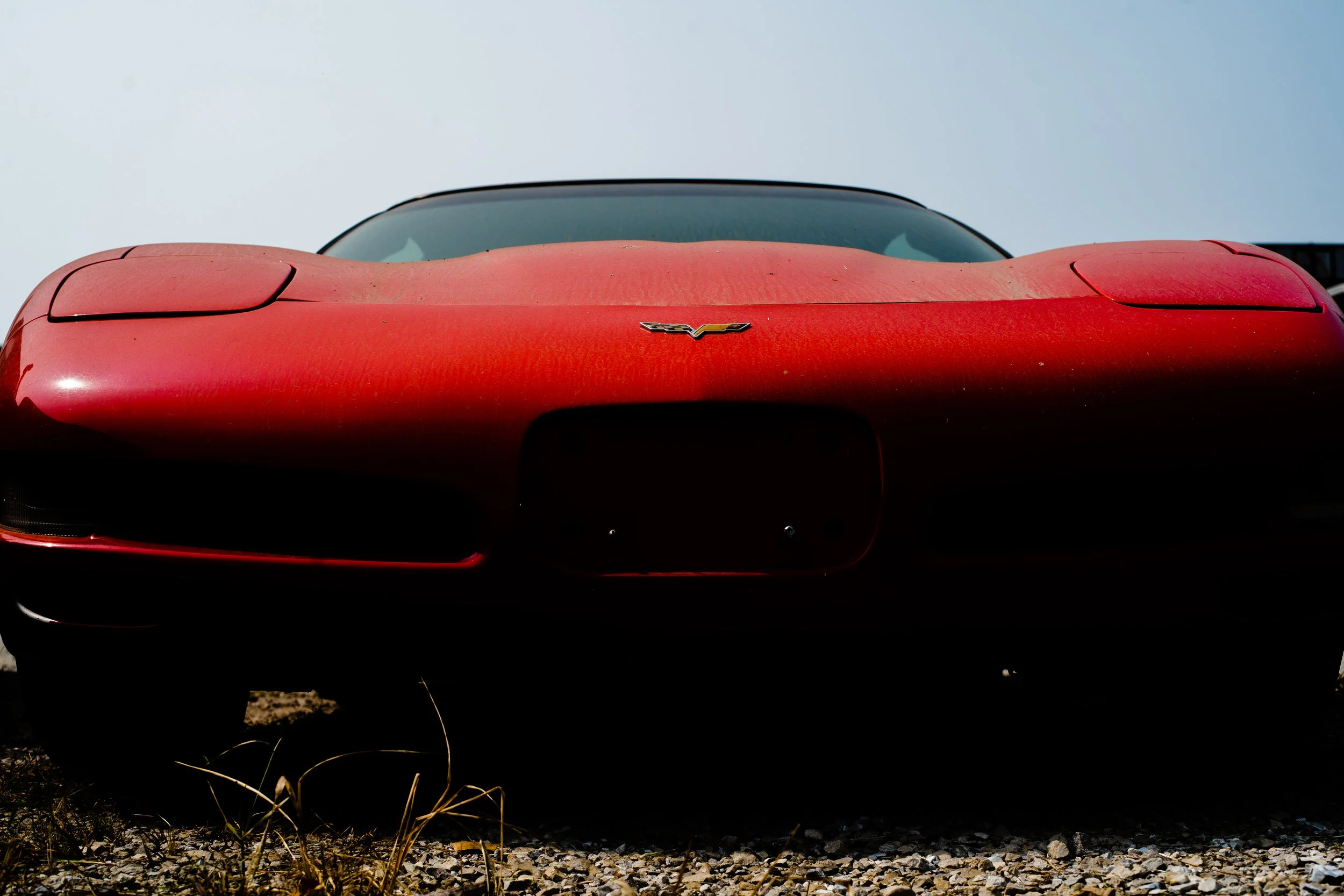 Close-up of front of red Chevrolet Corvette sports car parked on gravel with clear sky background.