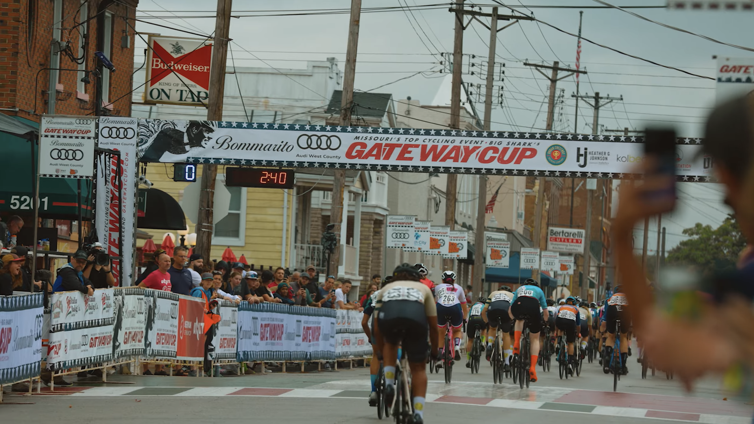 Cyclists racing in an organized cycling event with a crowd of spectators and banners along the street.