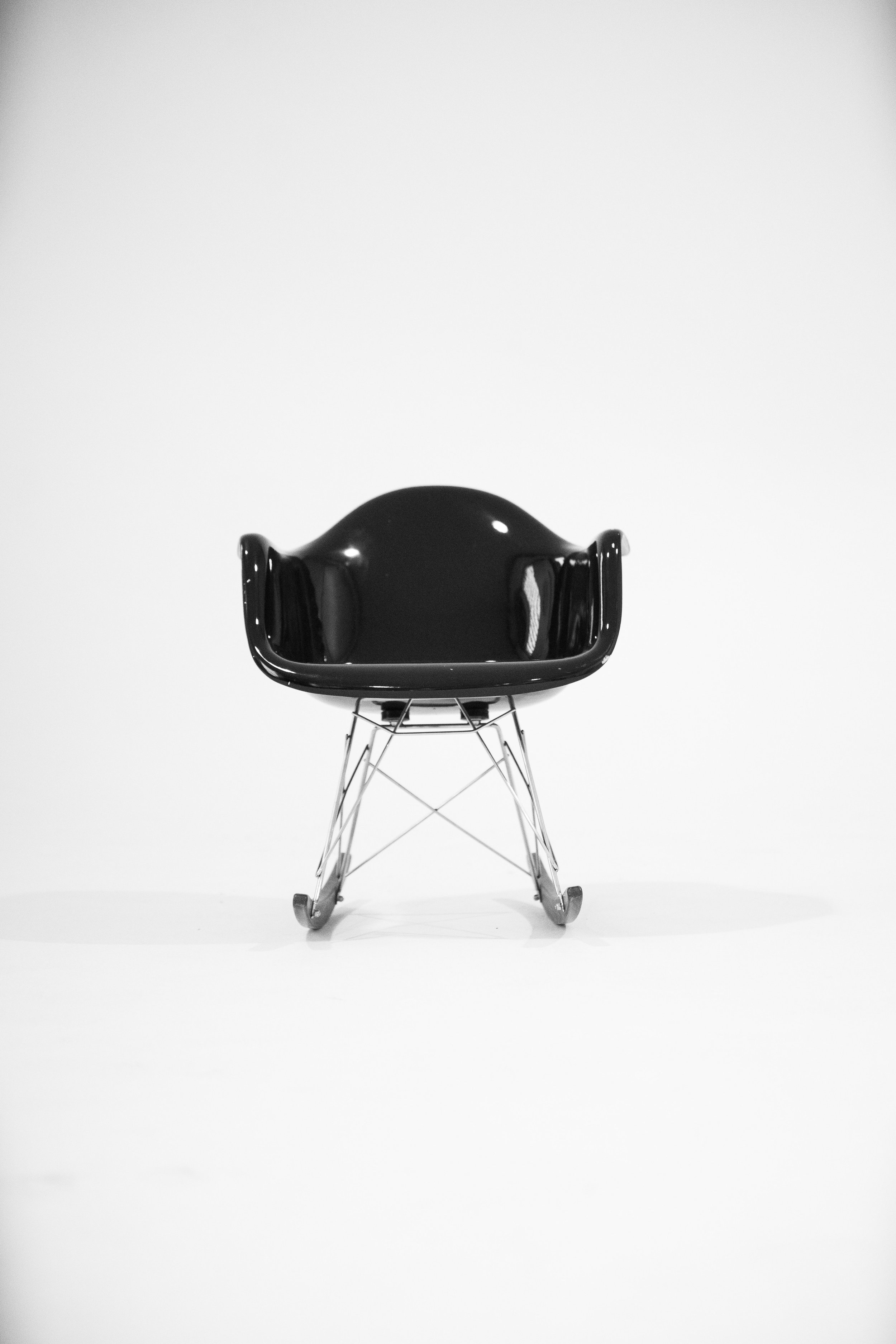 A black, modern chair with a plastic seat and metal wire base on wheels, positioned against a plain white background.
