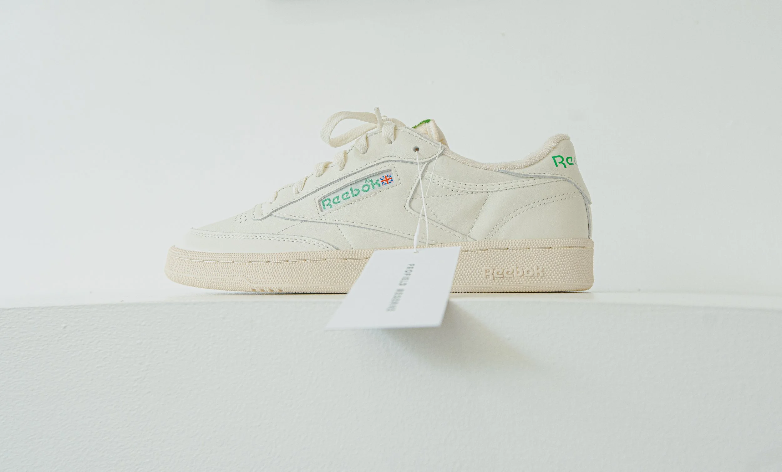 A white Reebok sneaker with green and blue accents on a white surface.