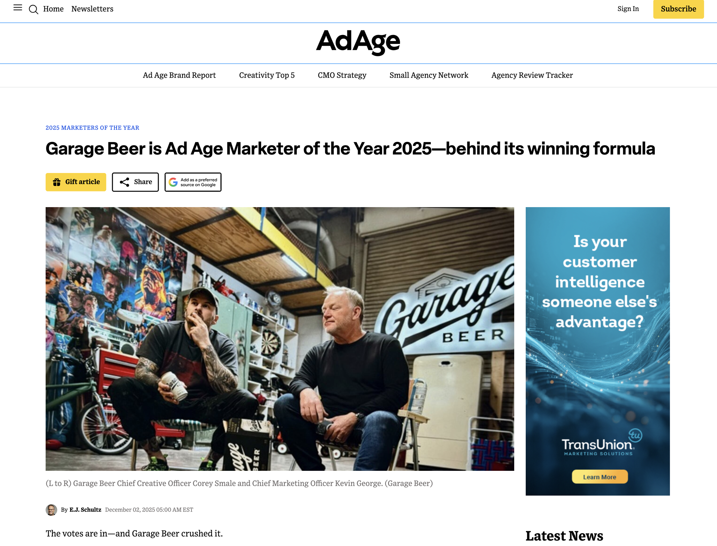 Two men sitting in a garage decorated with posters, engaged in conversation. One is holding a beer can and wearing a black shirt with tattoos on his arms, while the other is wearing a black long-sleeve shirt. The garage has an industrial ceiling with ductwork and a neon sign that reads 'Garage Beer'.