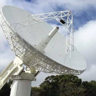 Large white satellite dish antenna pointed skyward against cloudy sky with trees below