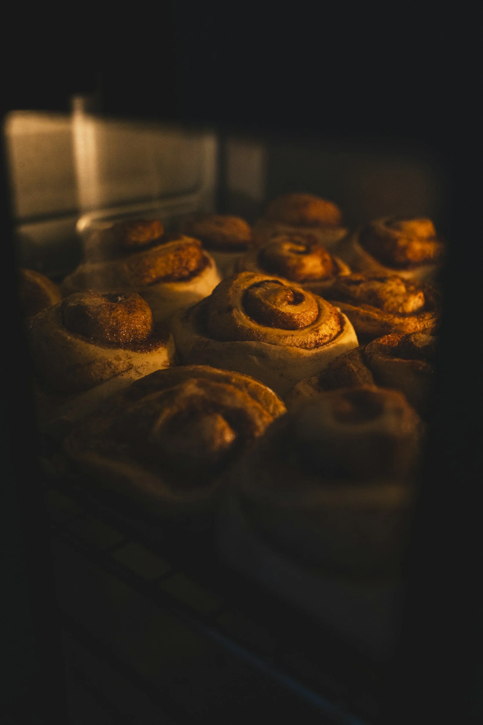 Cinnamon rolls baking in an oven with a warm glow.