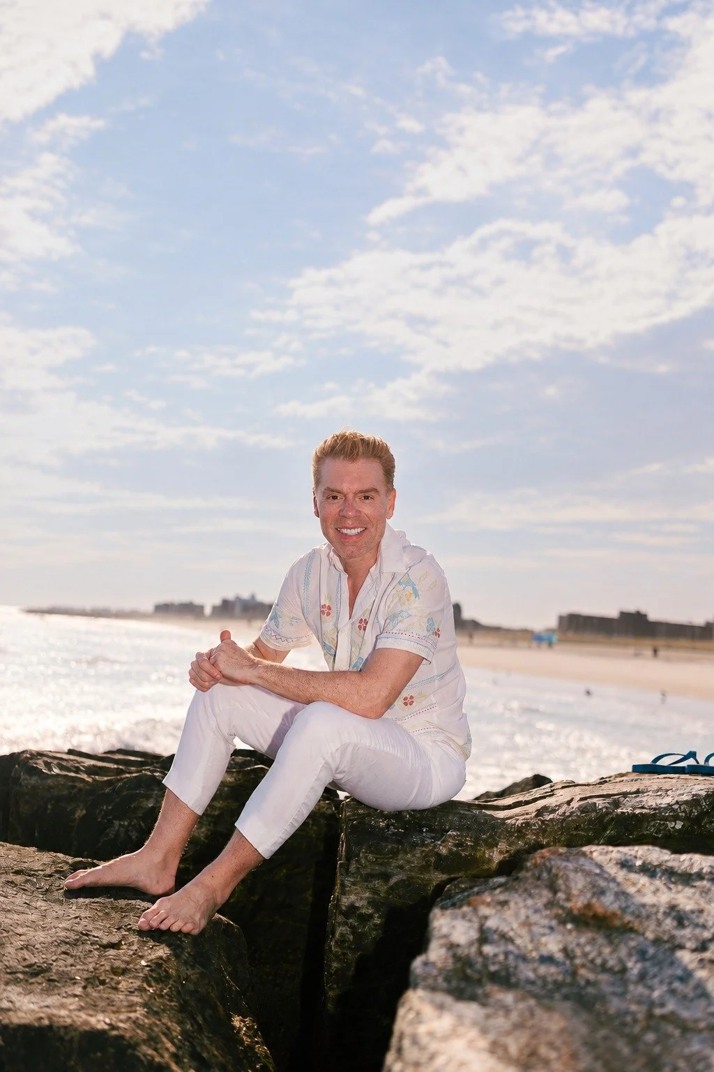 Antonio Moscoso Jr, hairstylist and founder of Agua Benta, sitting on the rocks by the ocean