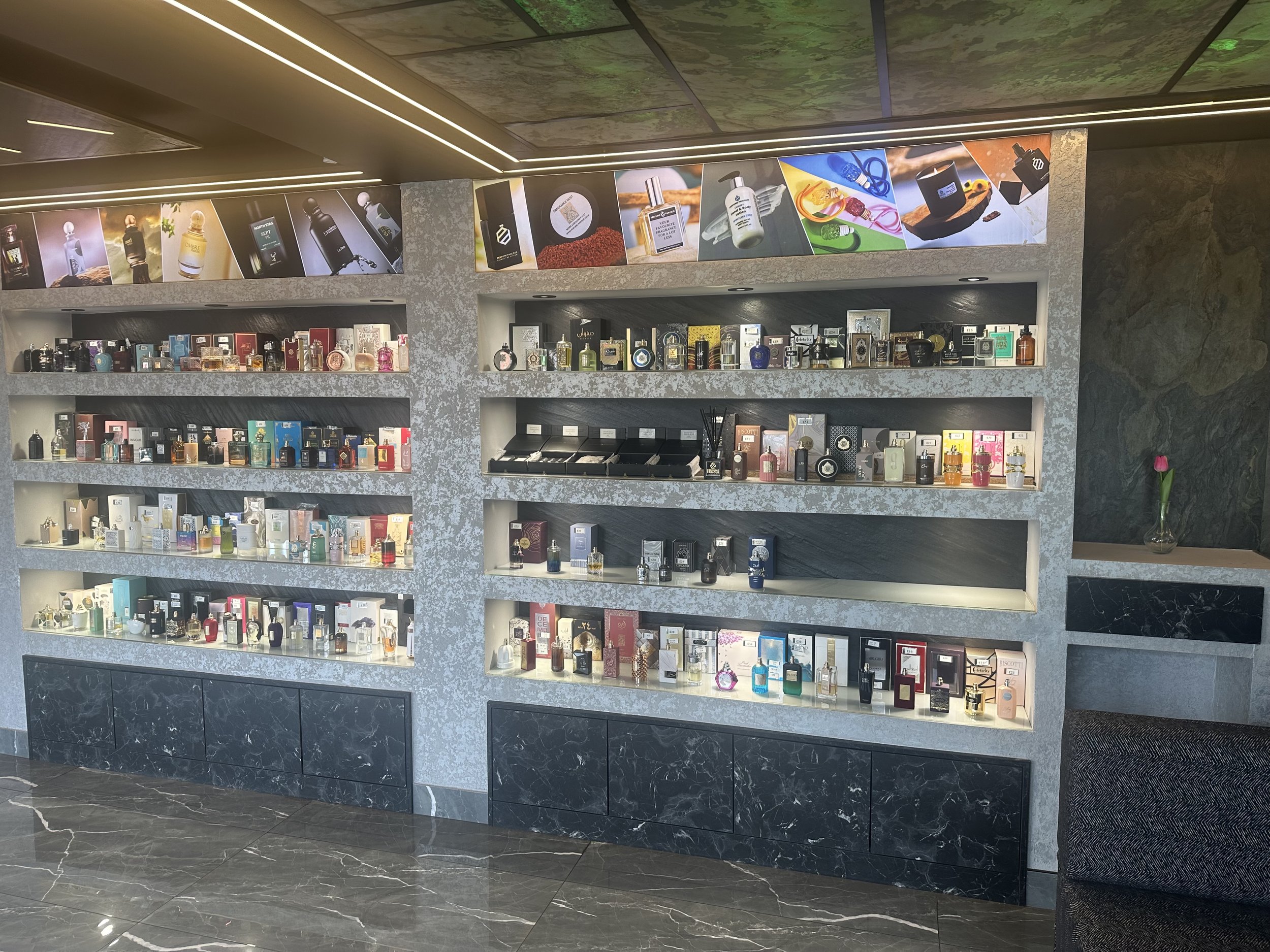 A display of perfume bottles arranged on shelves in a store, with large advertisements of perfume products on the upper part of the wall.