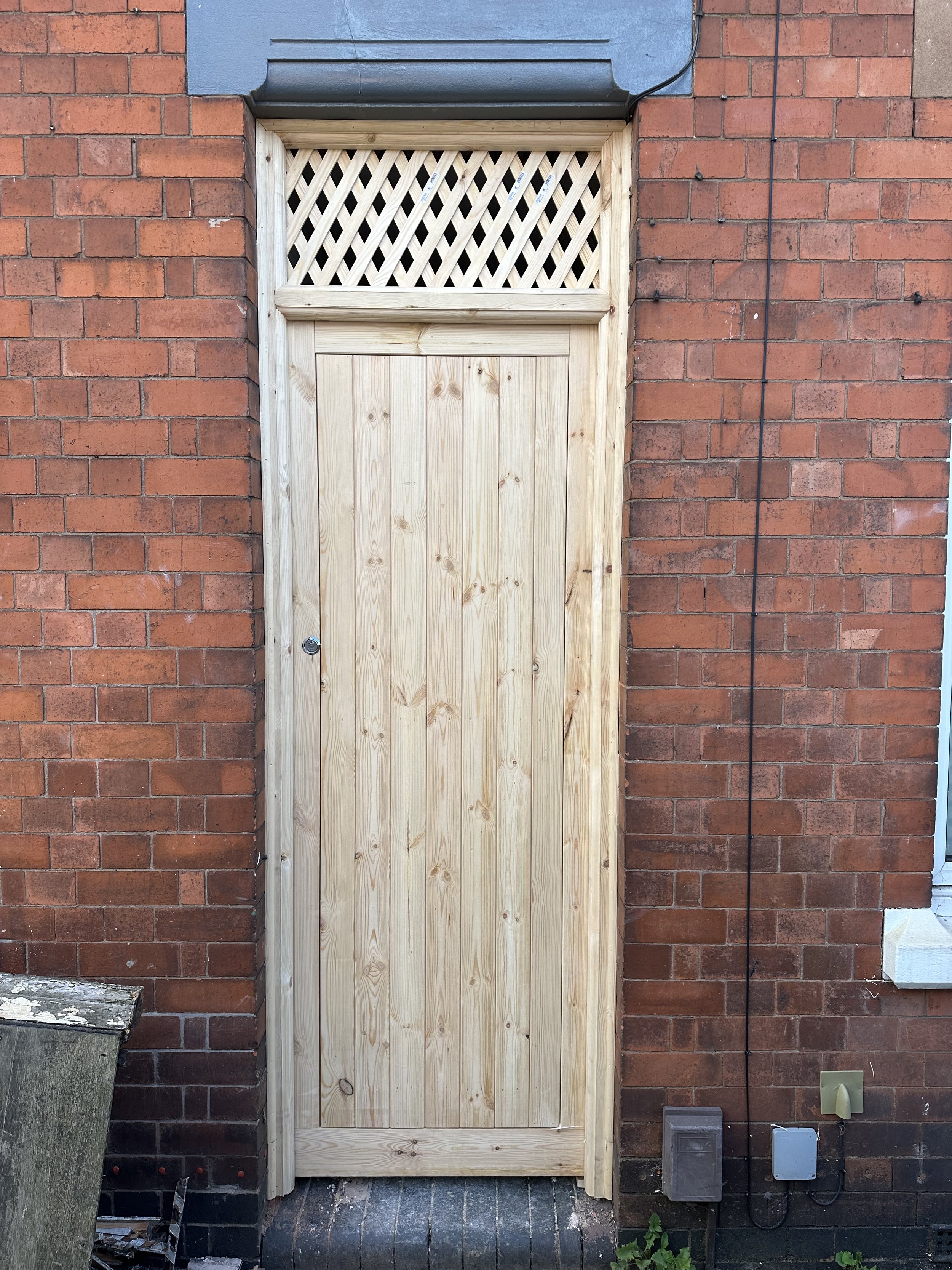 New wooden door with a lattice window installed in a brick wall.