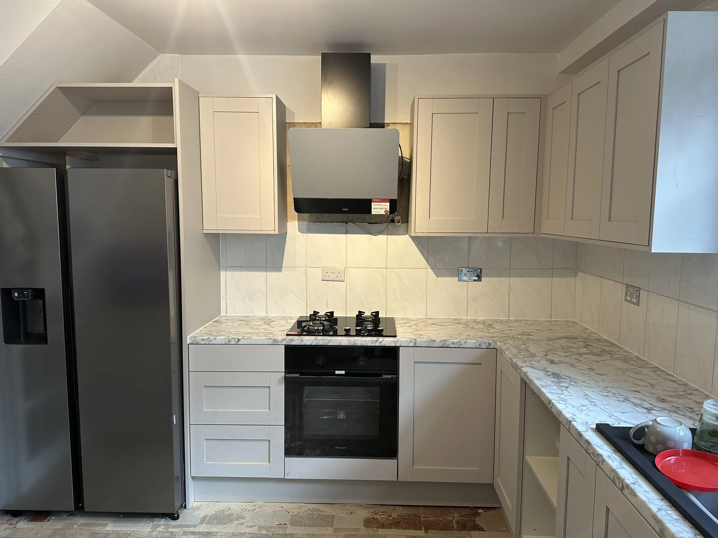 Kitchen with white cabinets, marble countertop, black oven and stove, and a gray refrigerator on the left. White tiled backsplash, wall outlets, and a window are visible on the right side.