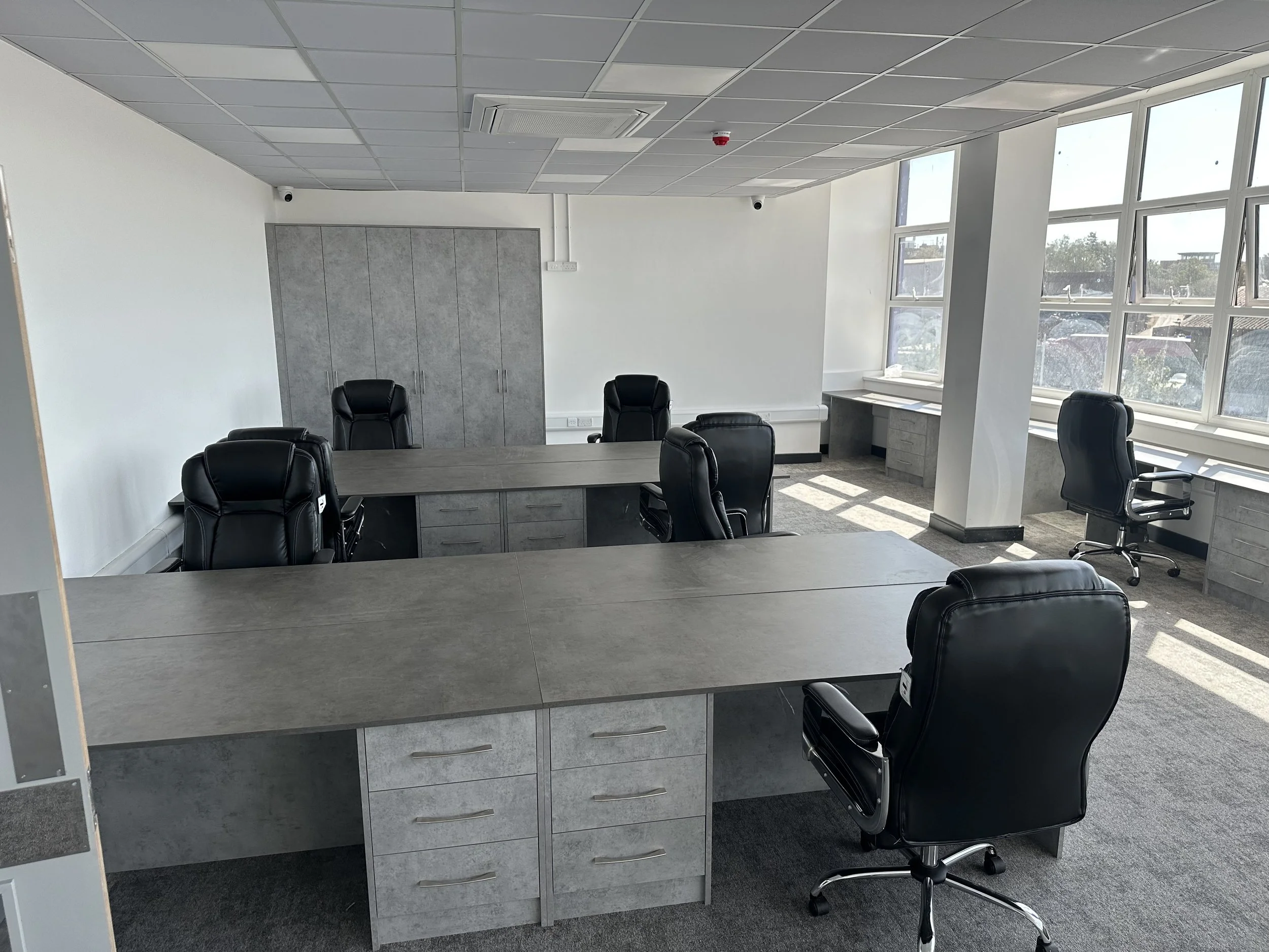 Empty modern conference room with large windows, black office chairs around a gray table, gray cabinets, and an air conditioning vent on the ceiling.