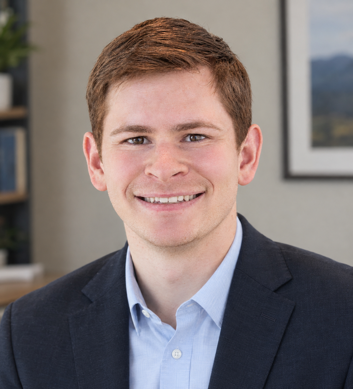 Professional headshot of a smiling man wearing a dark blazer and light blue dress shirt