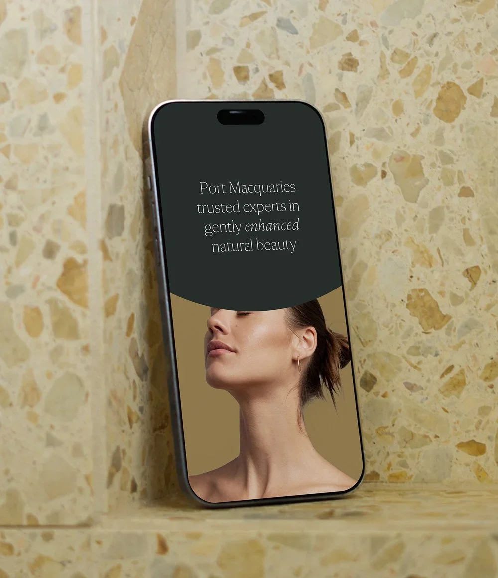 Smartphone displaying a natural beauty advertisement featuring a woman's portrait and the text “Port Macquarie’s trusted experts in gently enhanced natural beauty.”