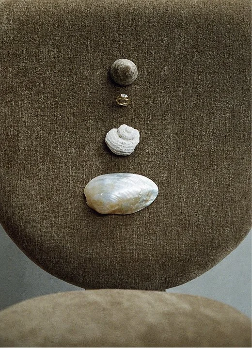 a picture of a Natalie Marie engagement ring styled with seashells on a green McMullin and Co dining chair
