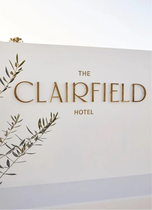 A picture of a white rendered concrete with a brass sign of The Clairfield Hotel