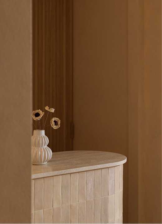 Sculptural white vase with dried flowers on a curved wood-paneled console table in a warm-toned interior