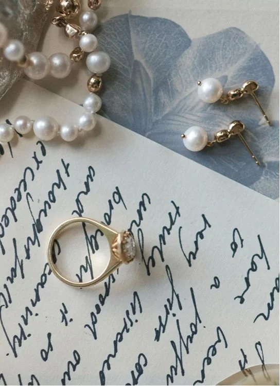 Gold ring, pearl earrings, and pearl bracelet arranged on handwritten paper and blue botanical stationery