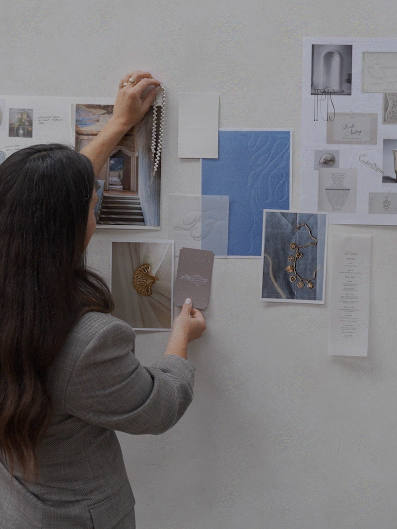 Designer arranging jewelry, fabric samples, and mood board images on a studio wall