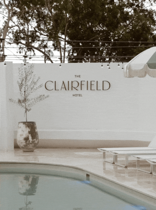 Poolside view of The Clairfield Hotel with lounge chairs, string lights, and a potted tree.