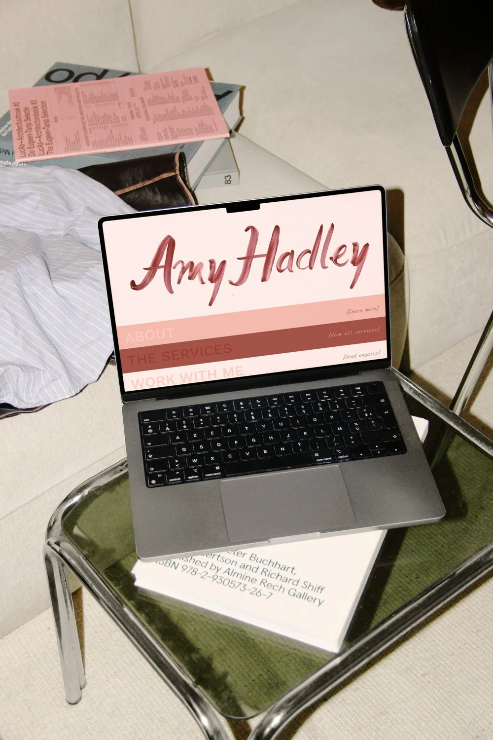 Laptop displaying the Amy Hadley website on a green chair beside books and a pink event program