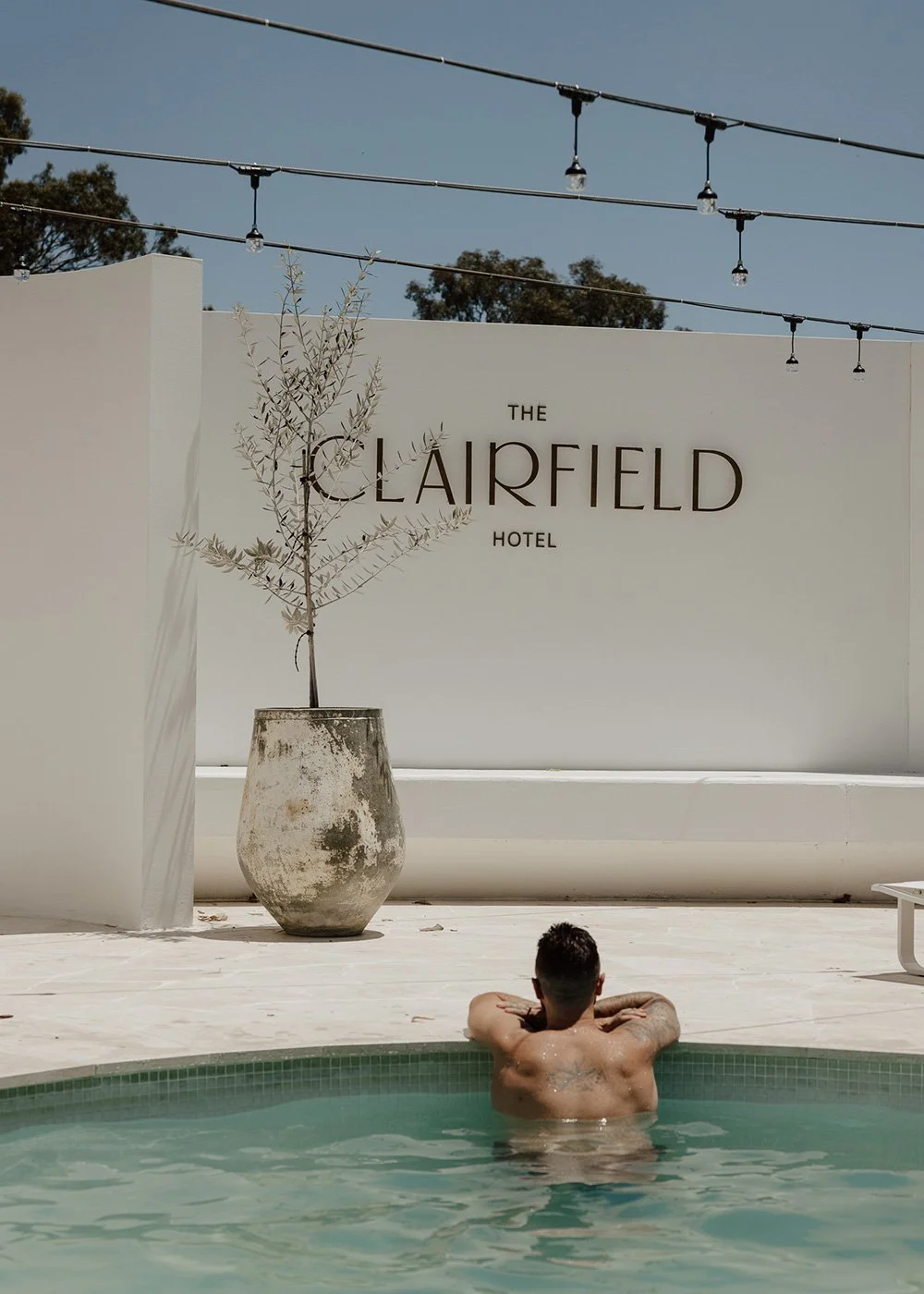 Man relaxing in a pool beneath string lights at The Clairfield Hotel