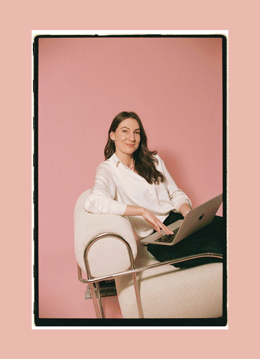 Woman using a laptop while sitting in a white armchair against a pink background