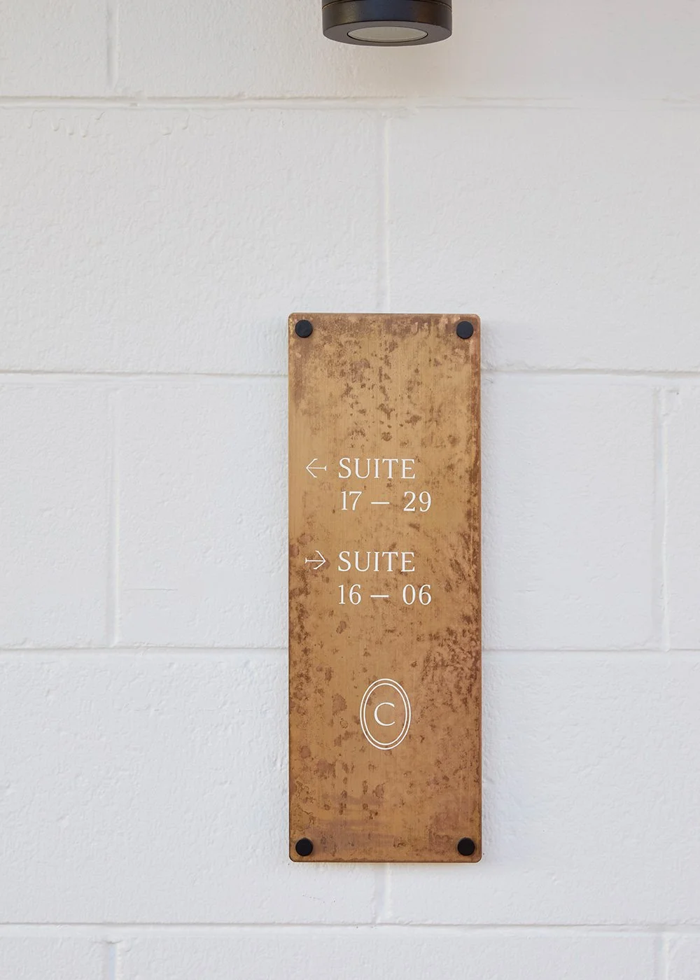 Bronze directional sign on a white brick wall pointing to suites 17–29 and 16–06.