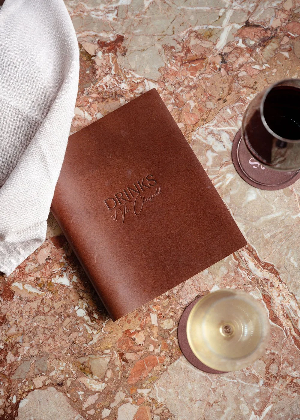 Leather drinks menu, wine glasses, and white napkin on a pink marble table