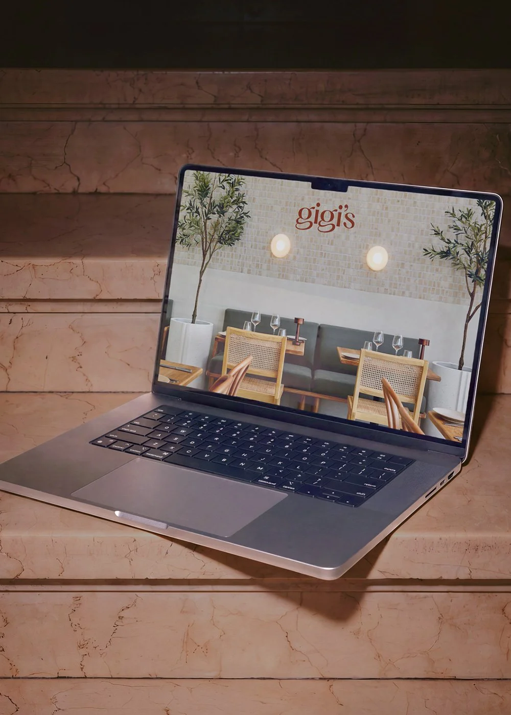 Open laptop displaying a restaurant interior with “gigi’s” branding on a marble staircase