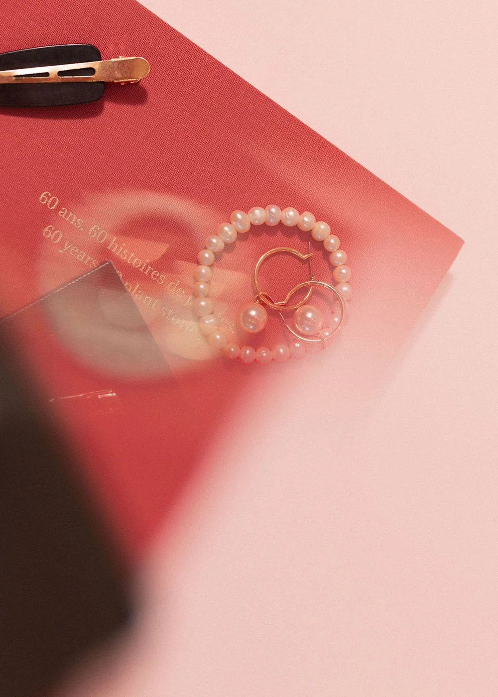 Pink pearl bracelet and gold hoop earrings on a red fashion magazine beside a hair clip