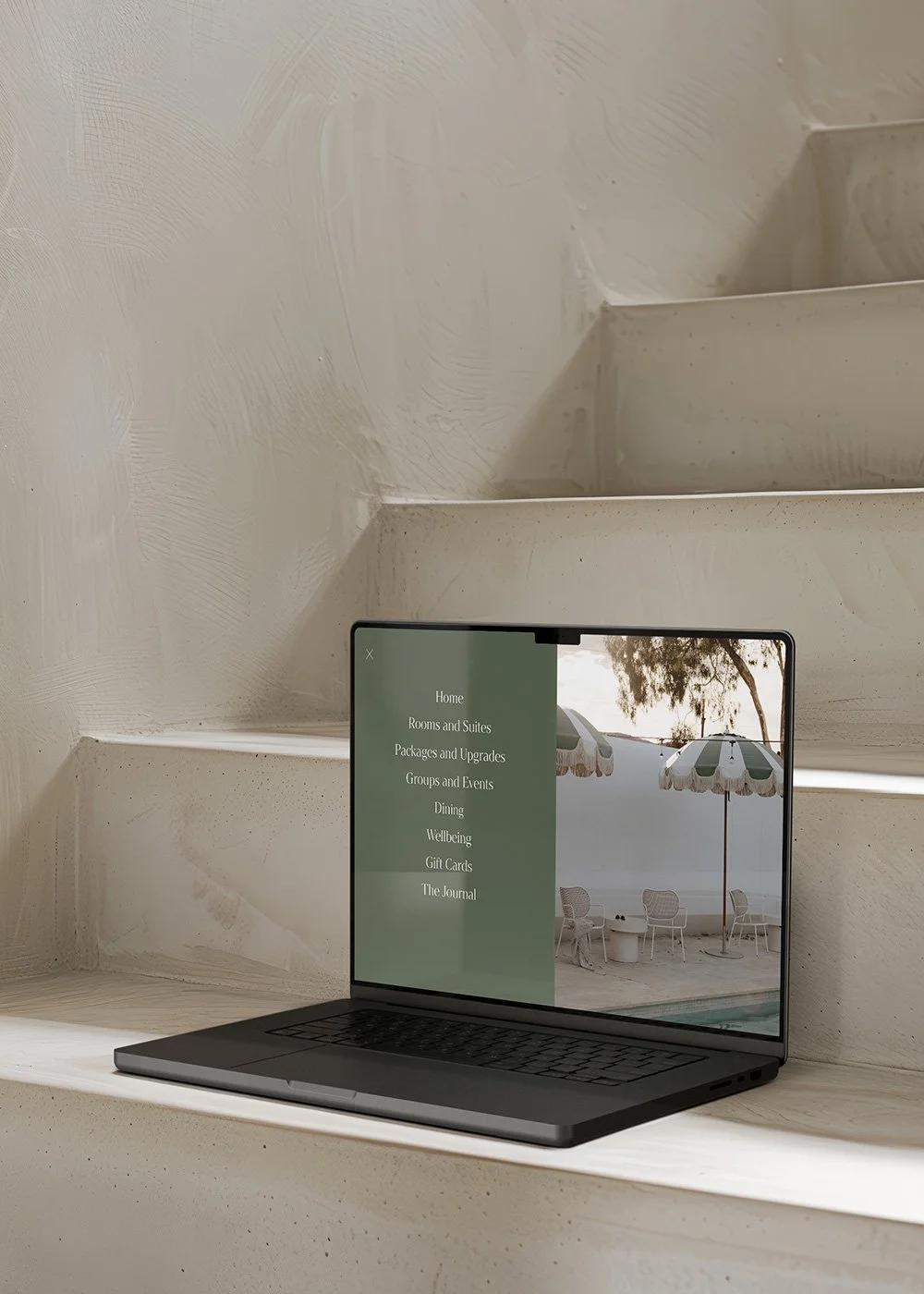 Black laptop displaying a resort website on white concrete stairs