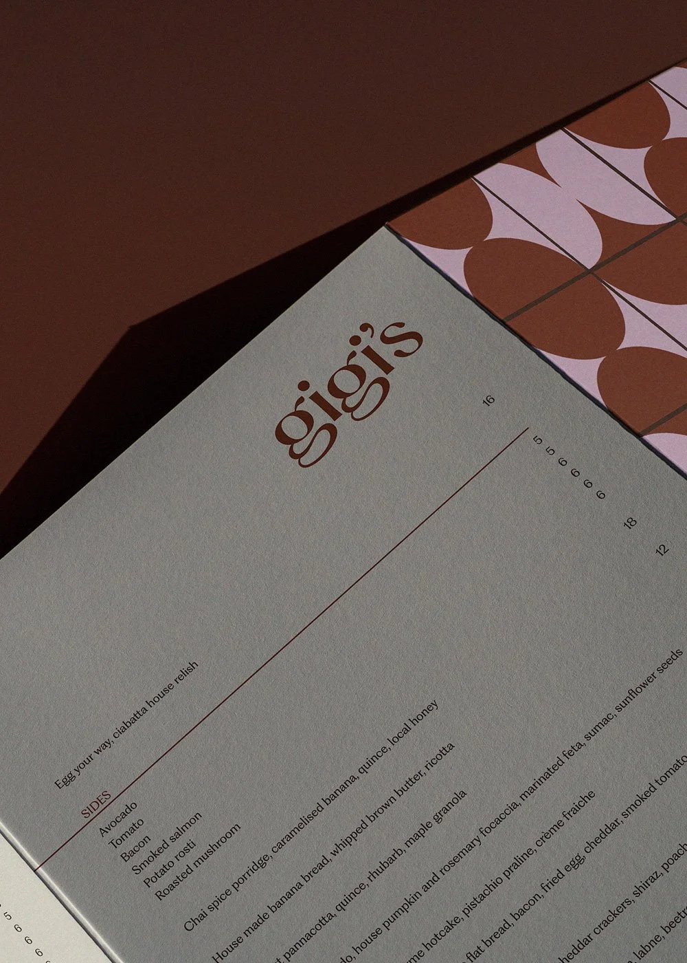 Close-up of a restaurant menu page listing side dishes, desserts, and ingredients beside a brown and pink patterned surface