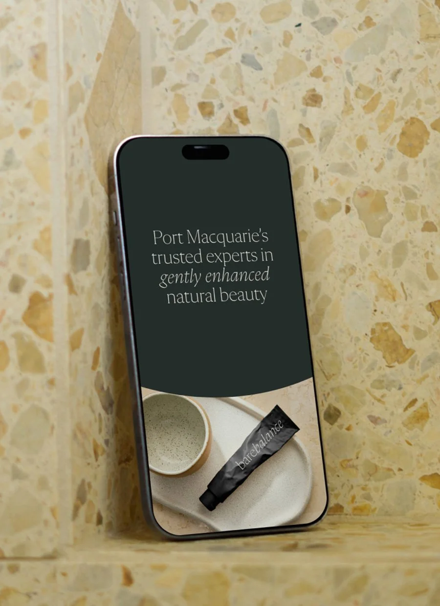 Smartphone displaying Port Macquarie beauty clinic branding and a Barebalm skincare tube on a ceramic tray.