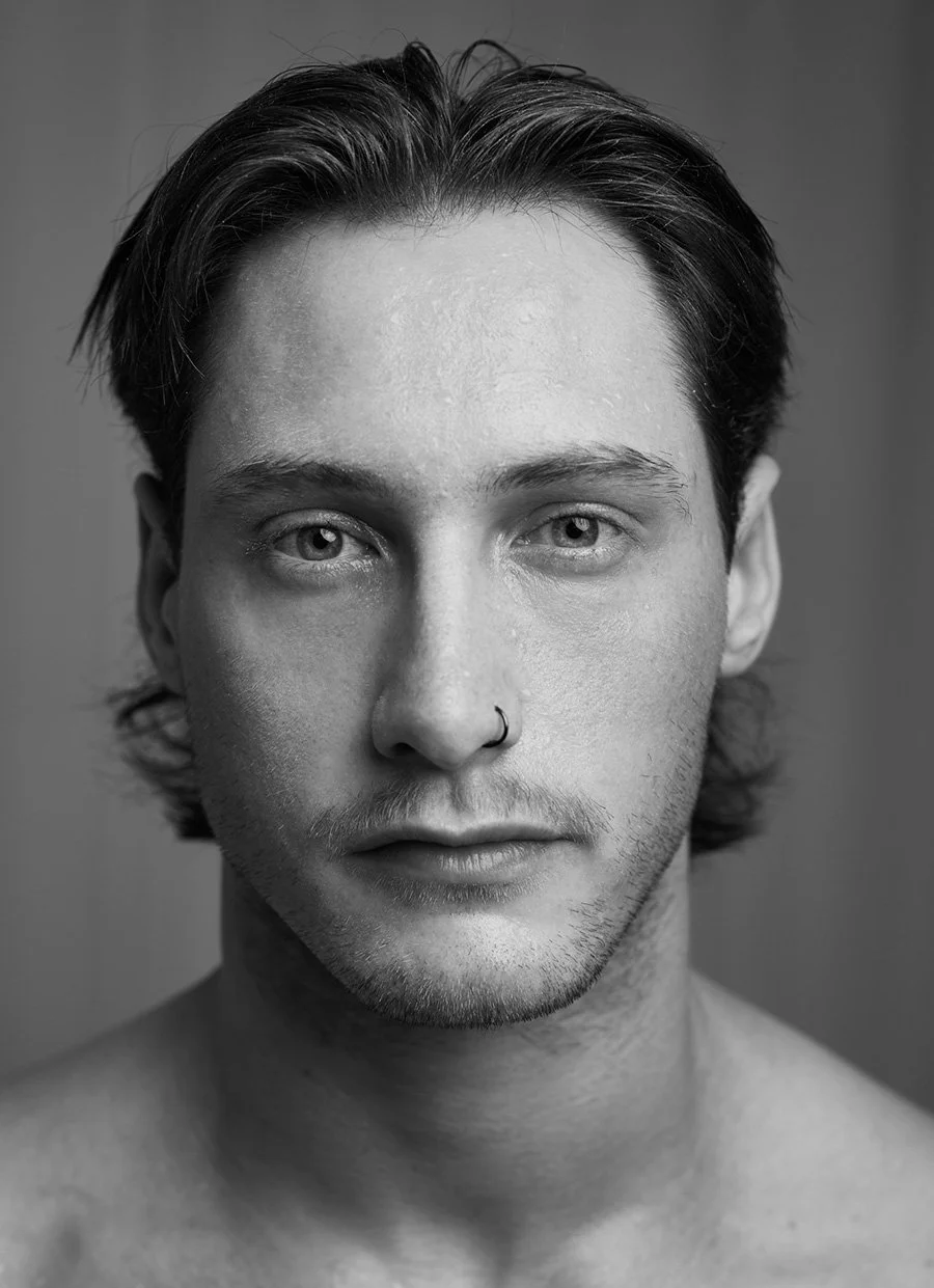 Black-and-white close-up portrait of a young man with dark hair, light stubble, and a nose ring