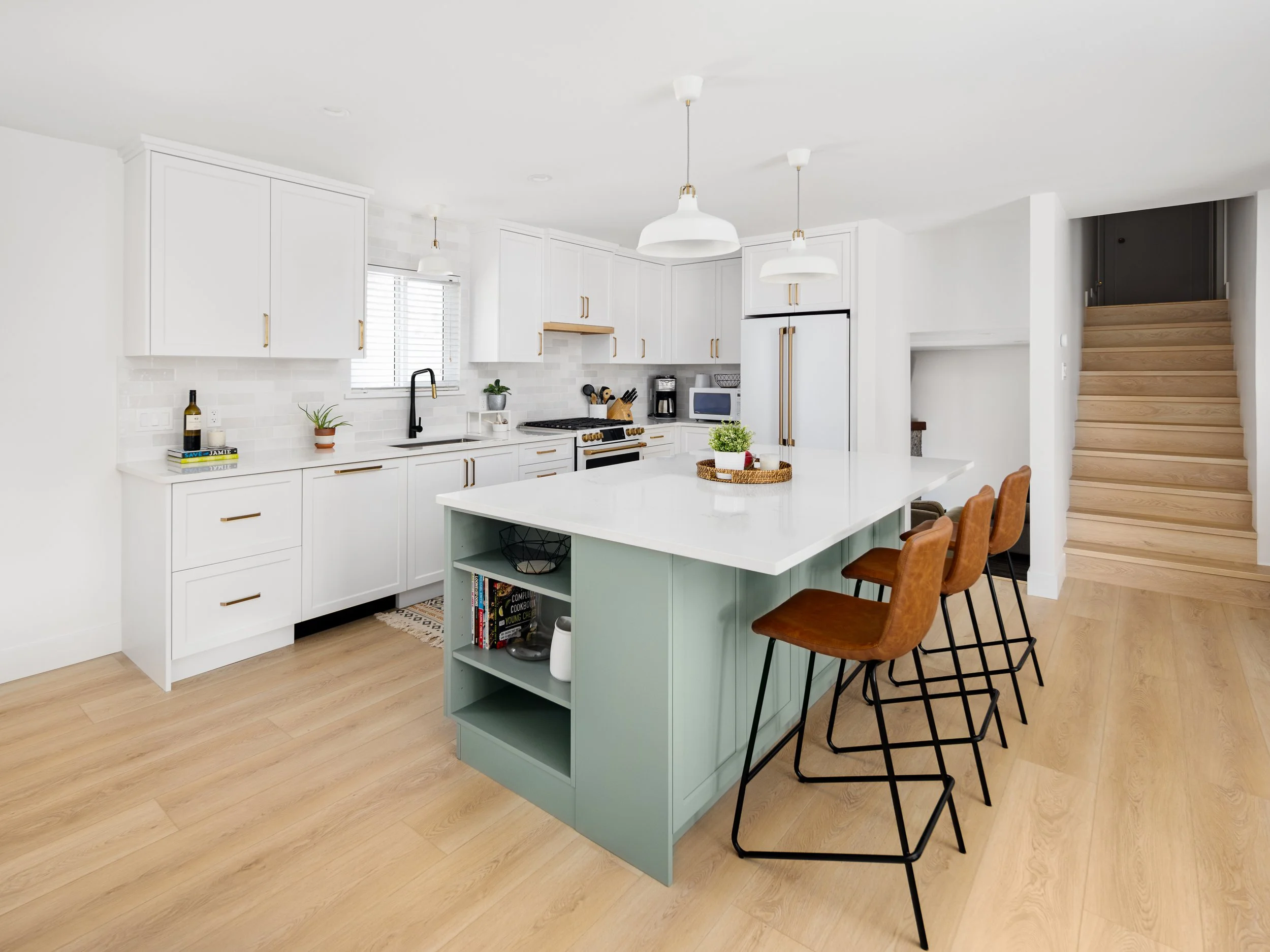 Bright residential kitchen with white cabinetry, sage island, brass hardware and natural wood flooring