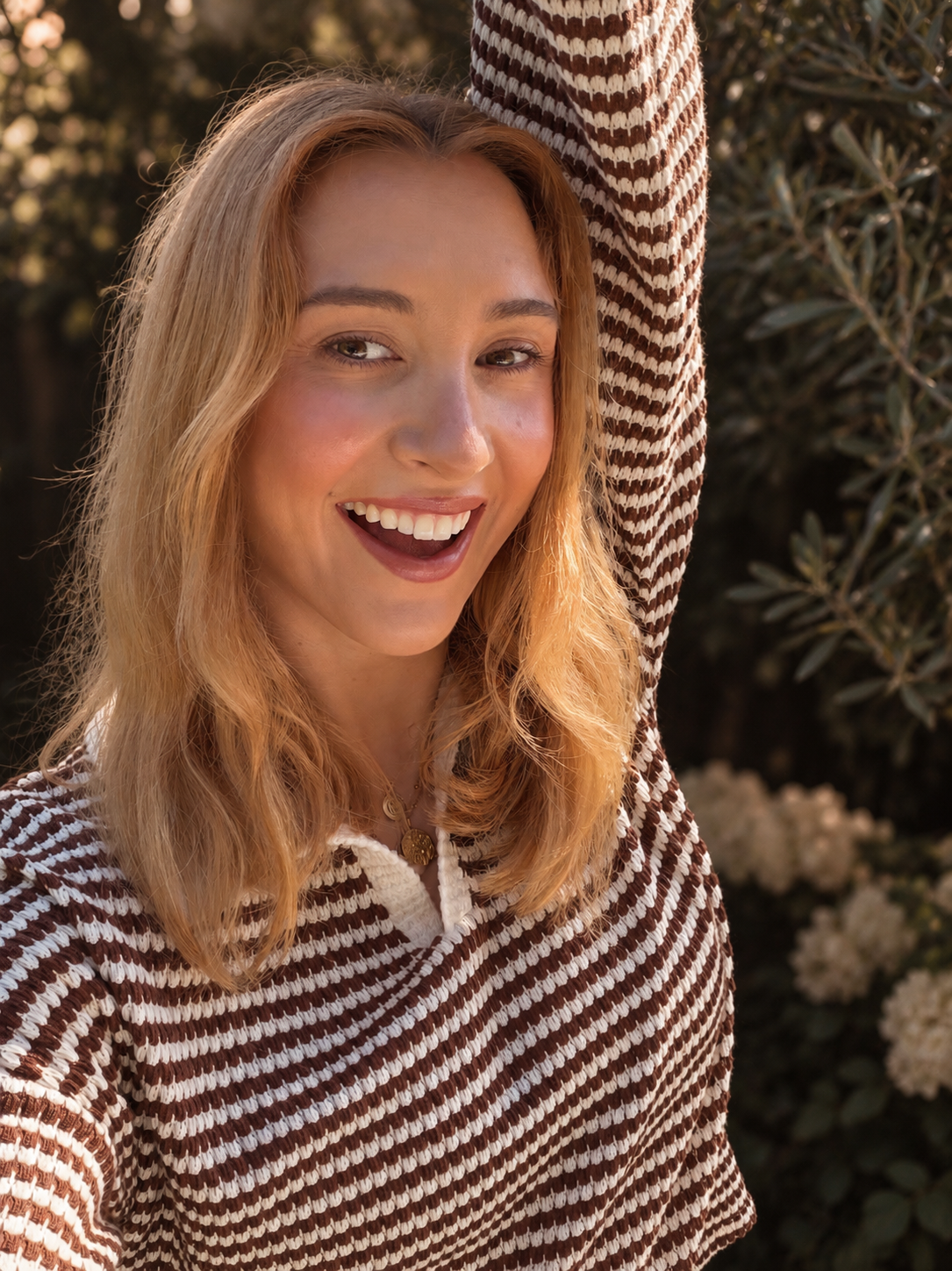 Smiling blonde woman wearing a brown-and-white striped knit hoodie outdoors