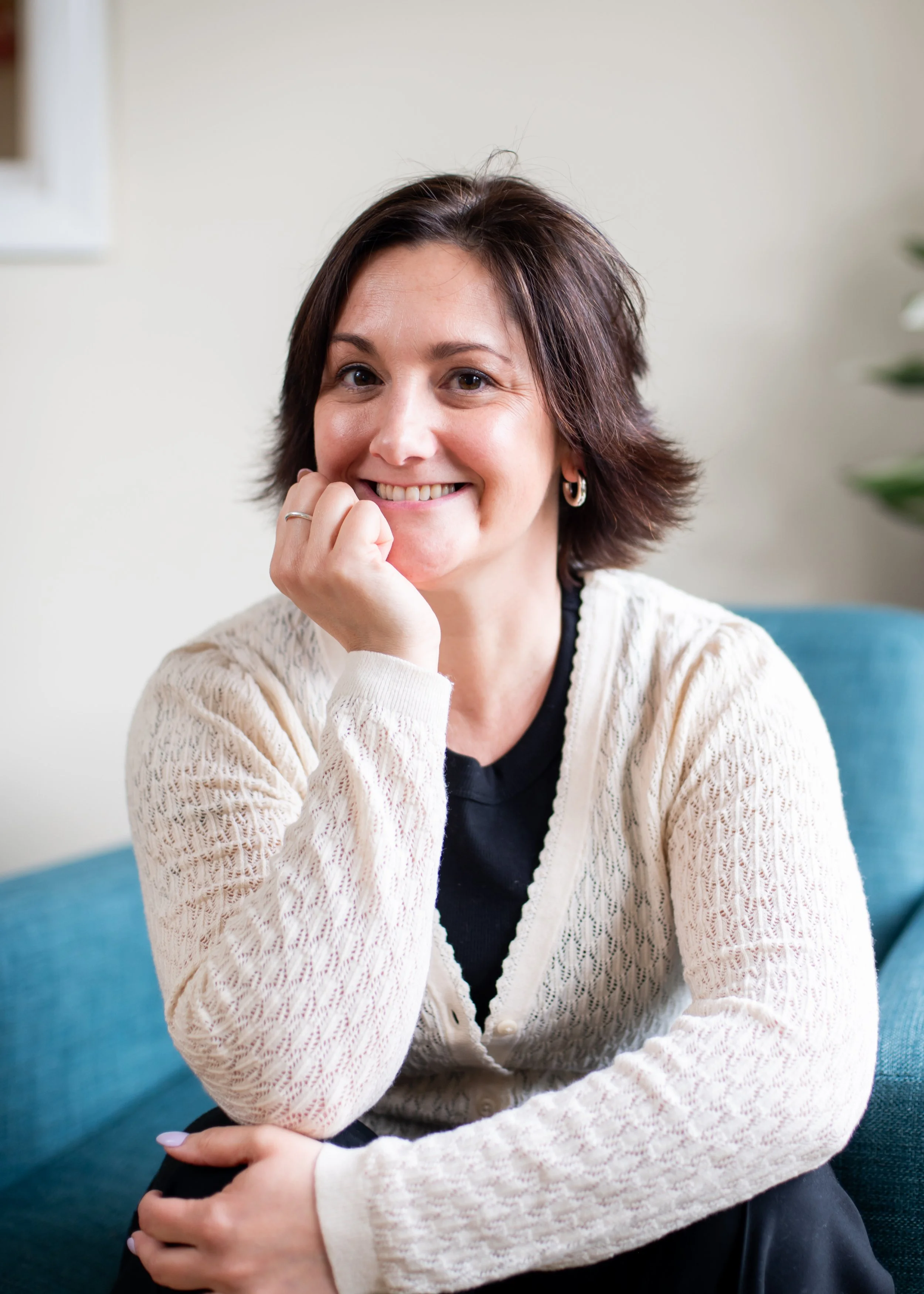 Smiling woman in a cream knit cardigan sitting on a blue sofa