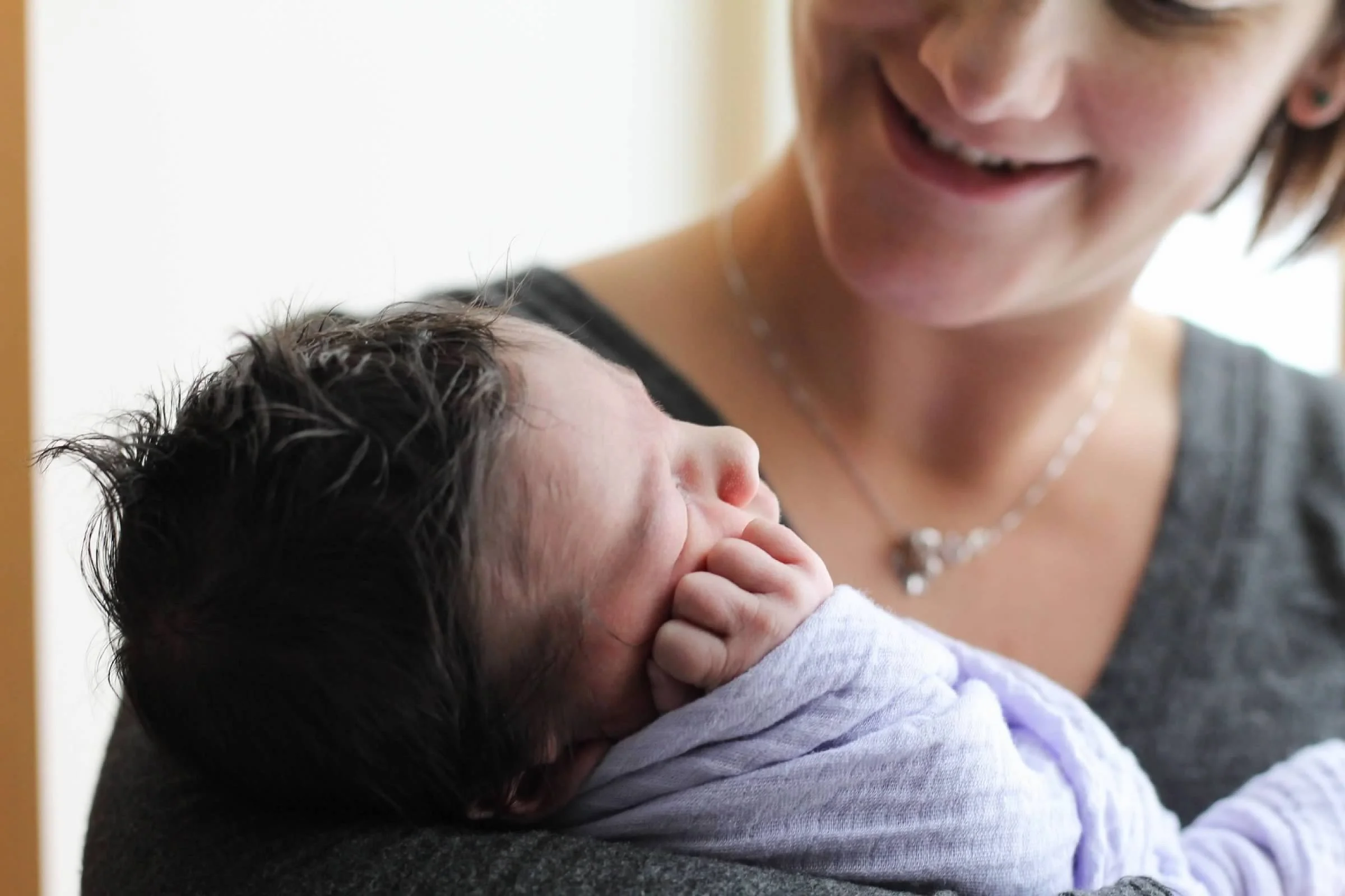 Woman holding a newborn baby with dark hair wrapped in a lavender blanket