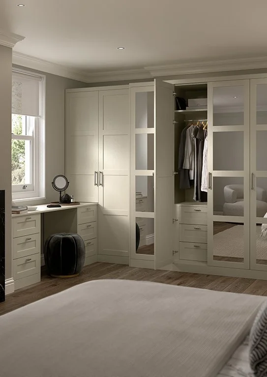 Bright bedroom with a built-in white wardrobe, mirrored closet doors, dressing table, window seat, and bed.