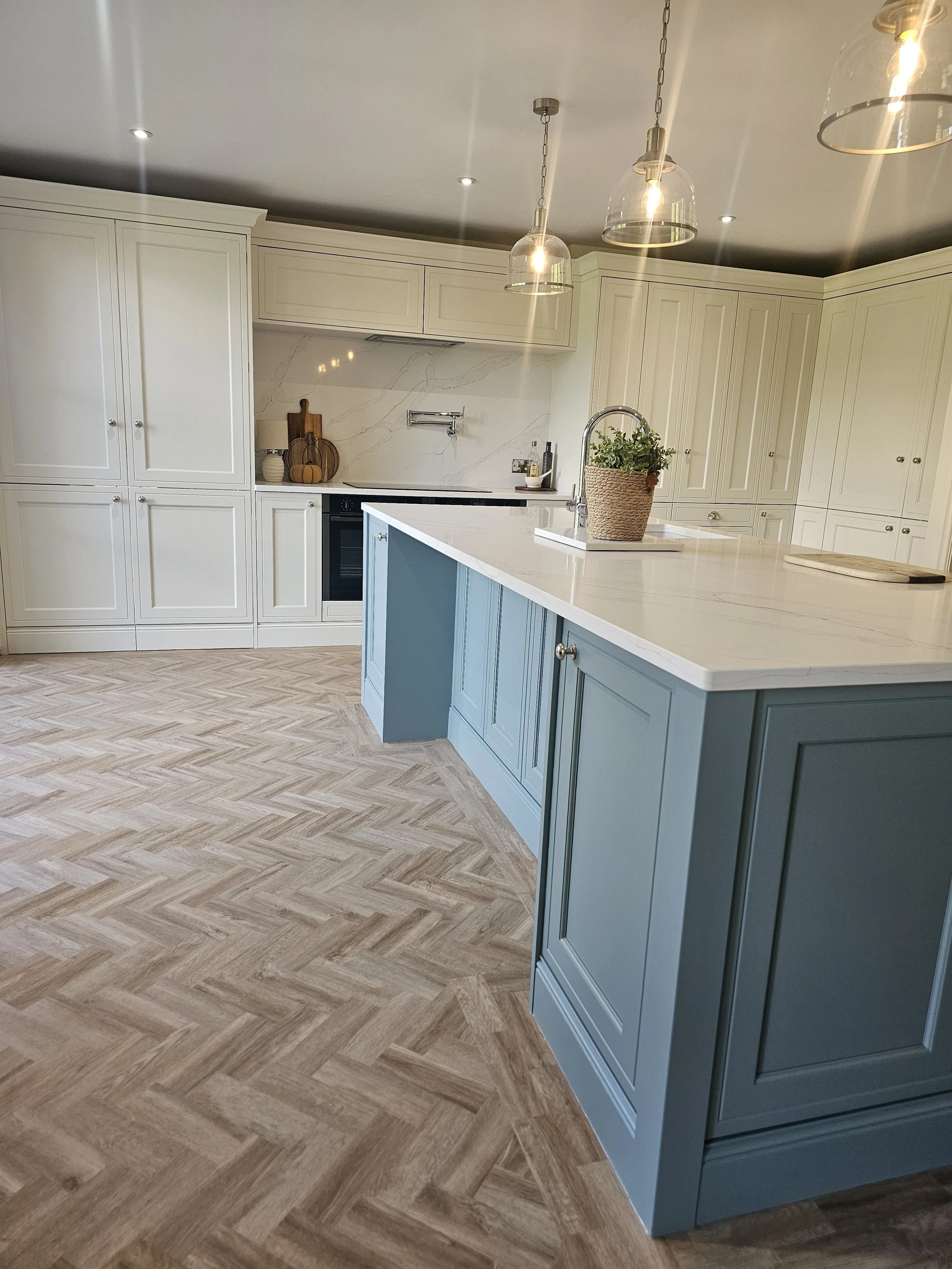 Modern kitchen with white cabinets, blue island, marble backsplash and countertops, pendant lights, and herringbone wood flooring