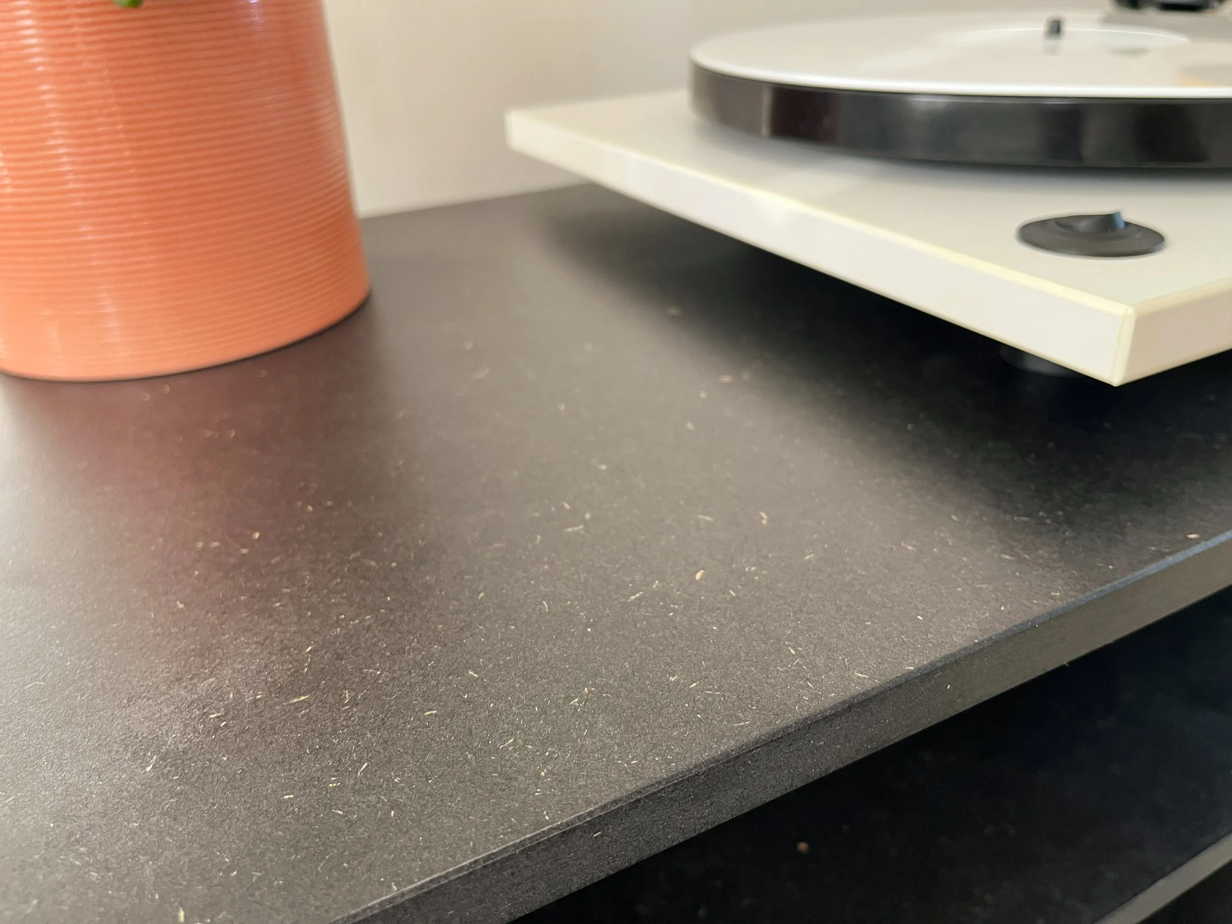 Close-up of a dark grey countertop with a reddish-orange textured container on the left and a record player on the right.