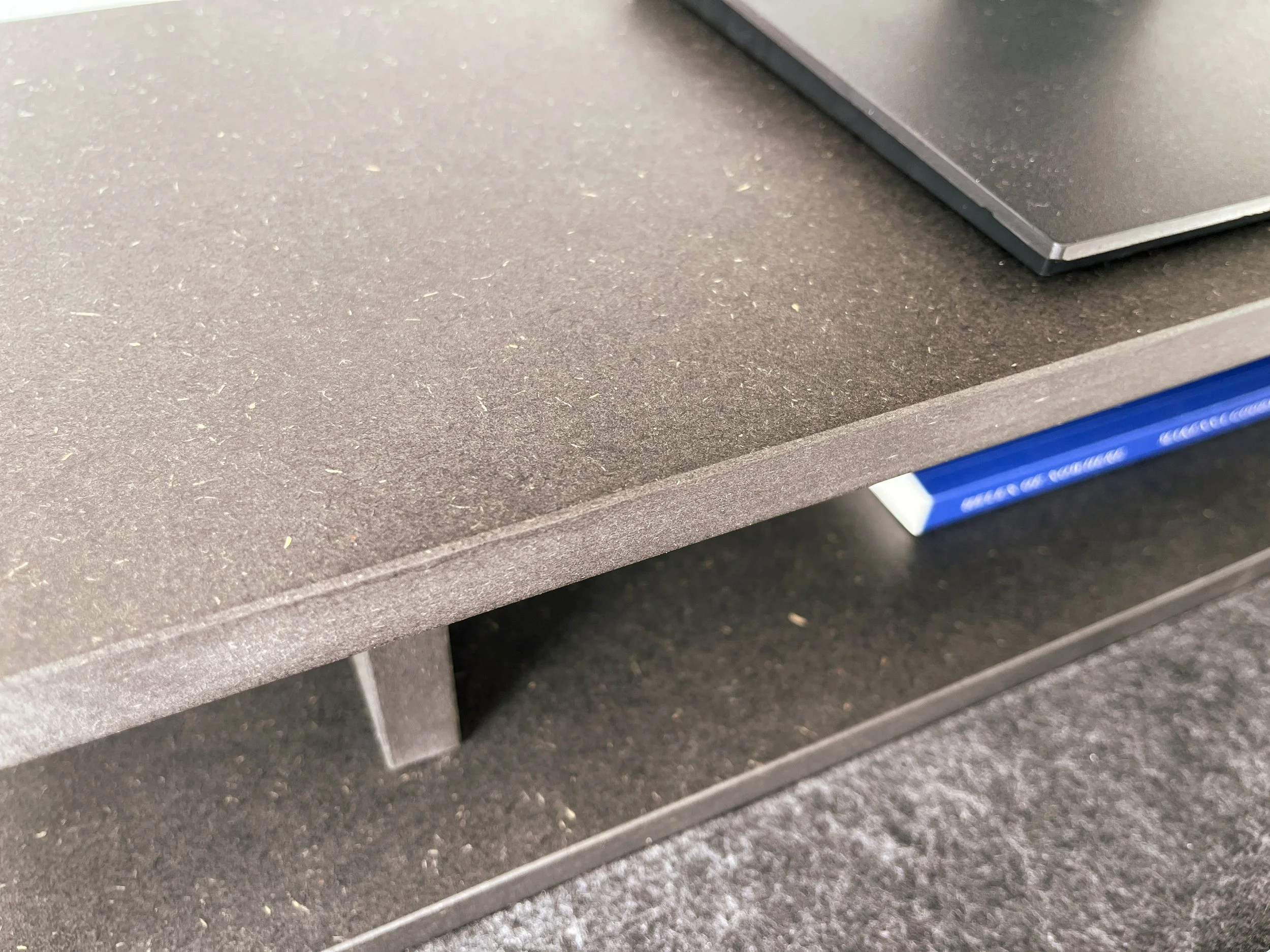 Close-up view of a computer laptop resting on a grey desk with a textured surface, with a small part of a blue drawer visible underneath.