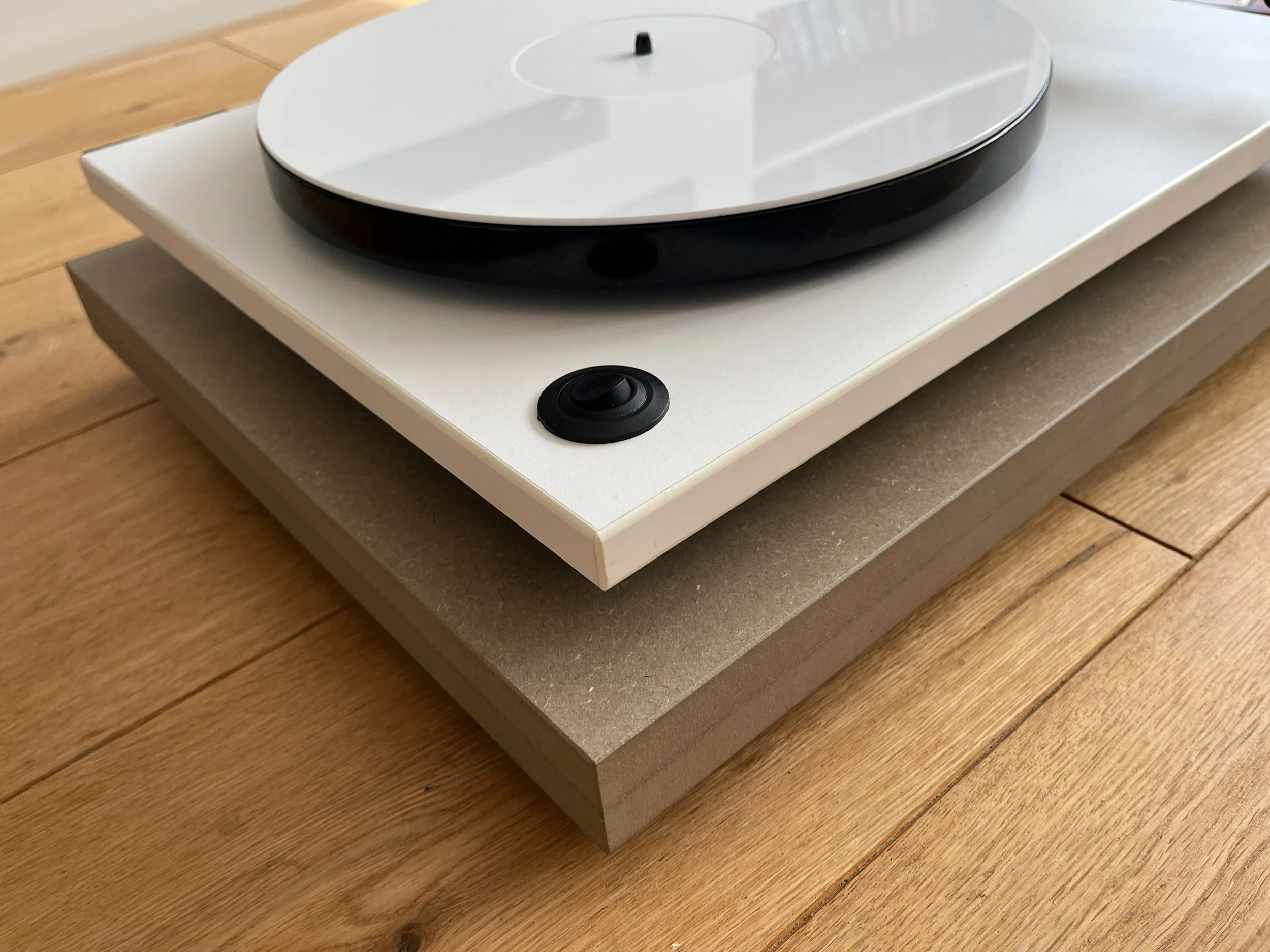 A modern white and black turntable on a white stand, placed on a wooden table.