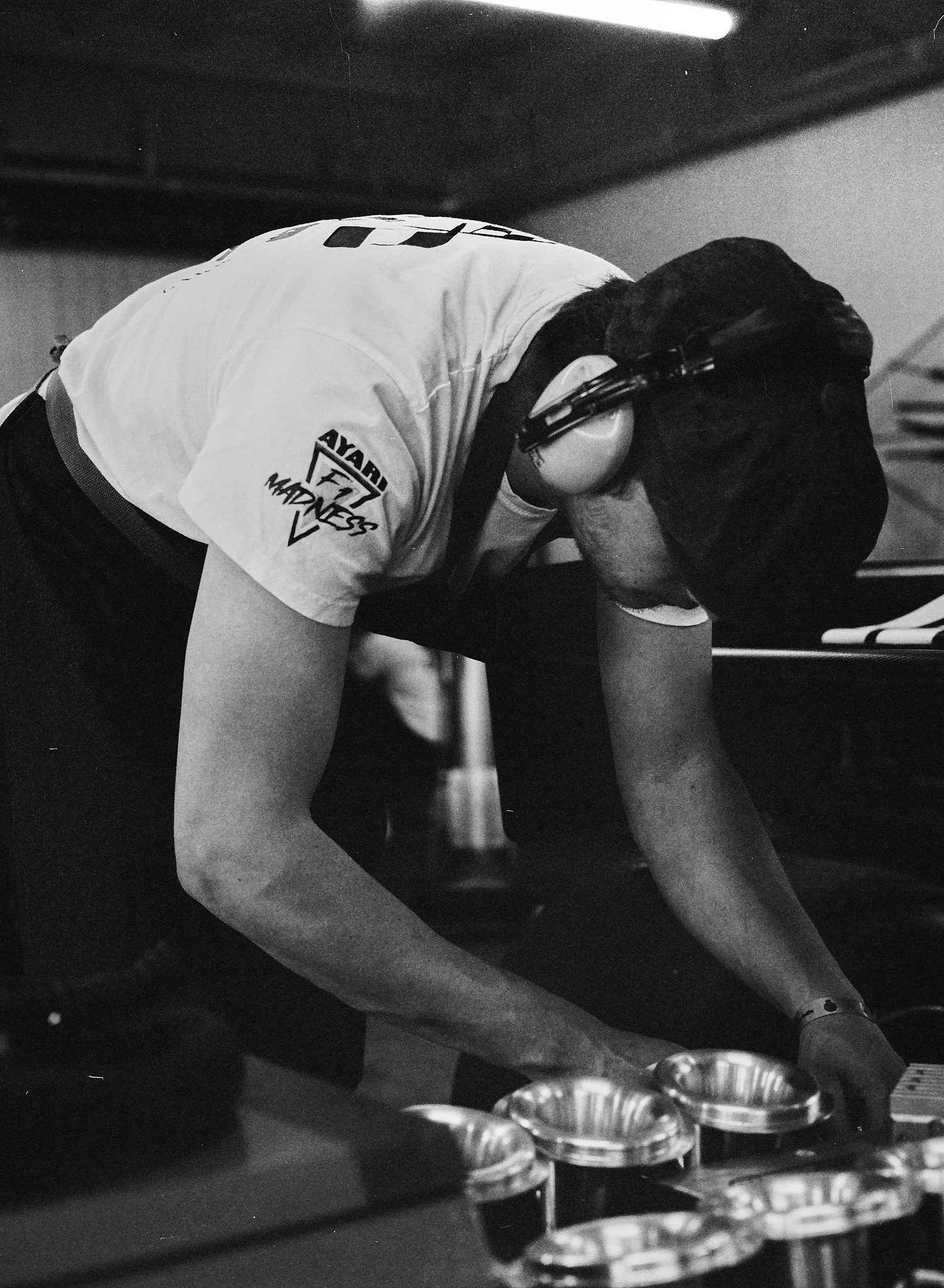 A person wearing a white sports jersey and protective gloves preparing to place or remove metal molds from an oven or kiln, likely for baking or industrial purposes.