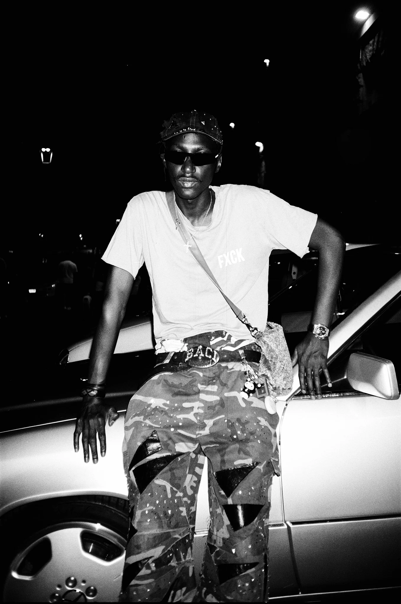 A young person wearing sunglasses, a baseball cap, a white t-shirt with 