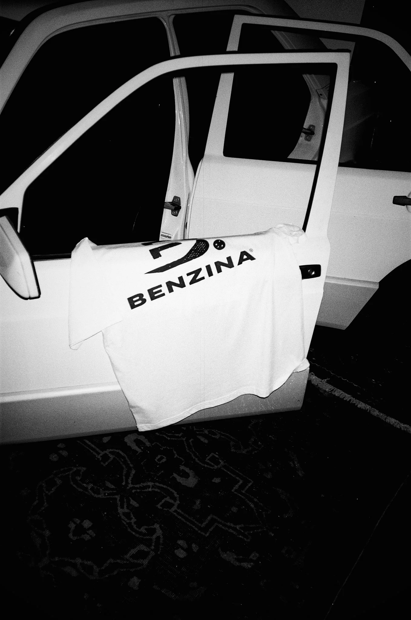 A white vehicle with a banner or cloth hanging from the side that has the words "BENZINA" and a logo. The vehicle's door is open, revealing the interior.