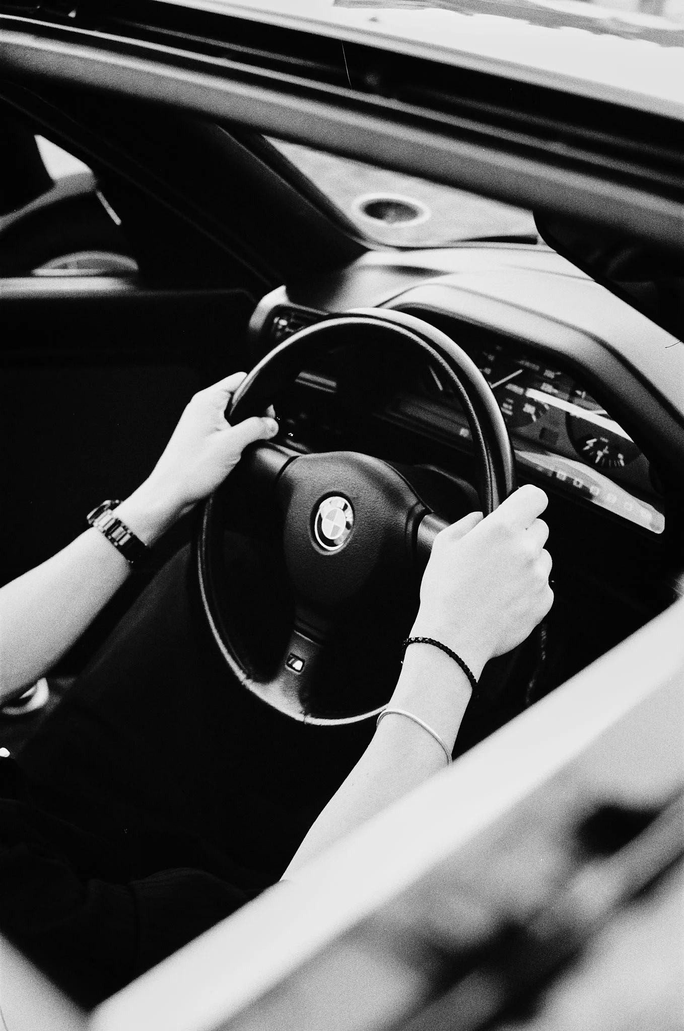 Black and white photo of a person holding a steering wheel of a BMW vehicle with dashboard visible in the background.