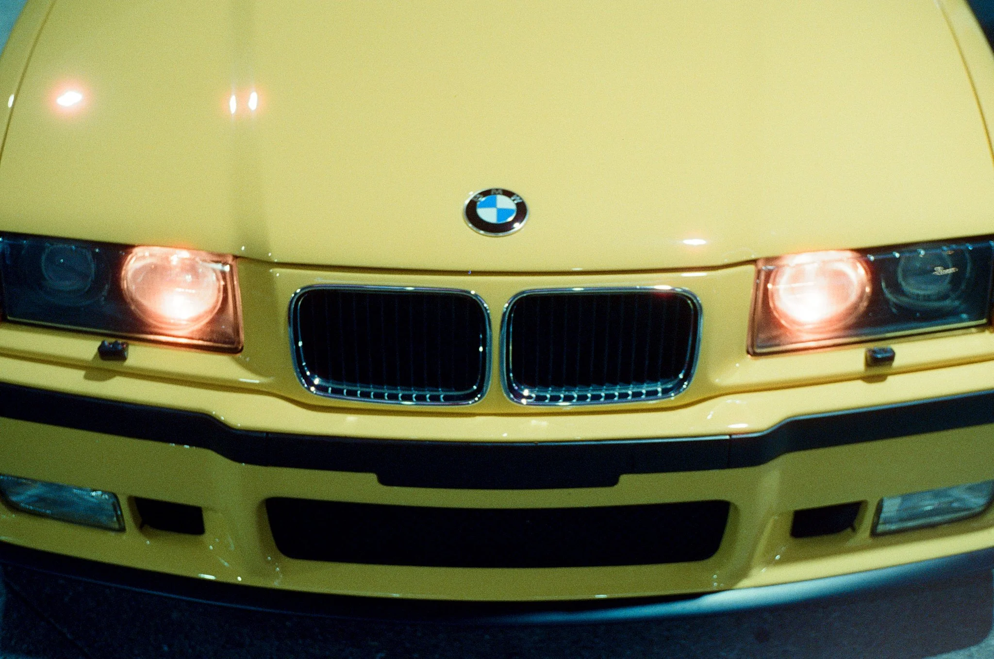 Close-up of the front of a yellow BMW car, showing the headlights, grille, and the BMW logo on the hood.