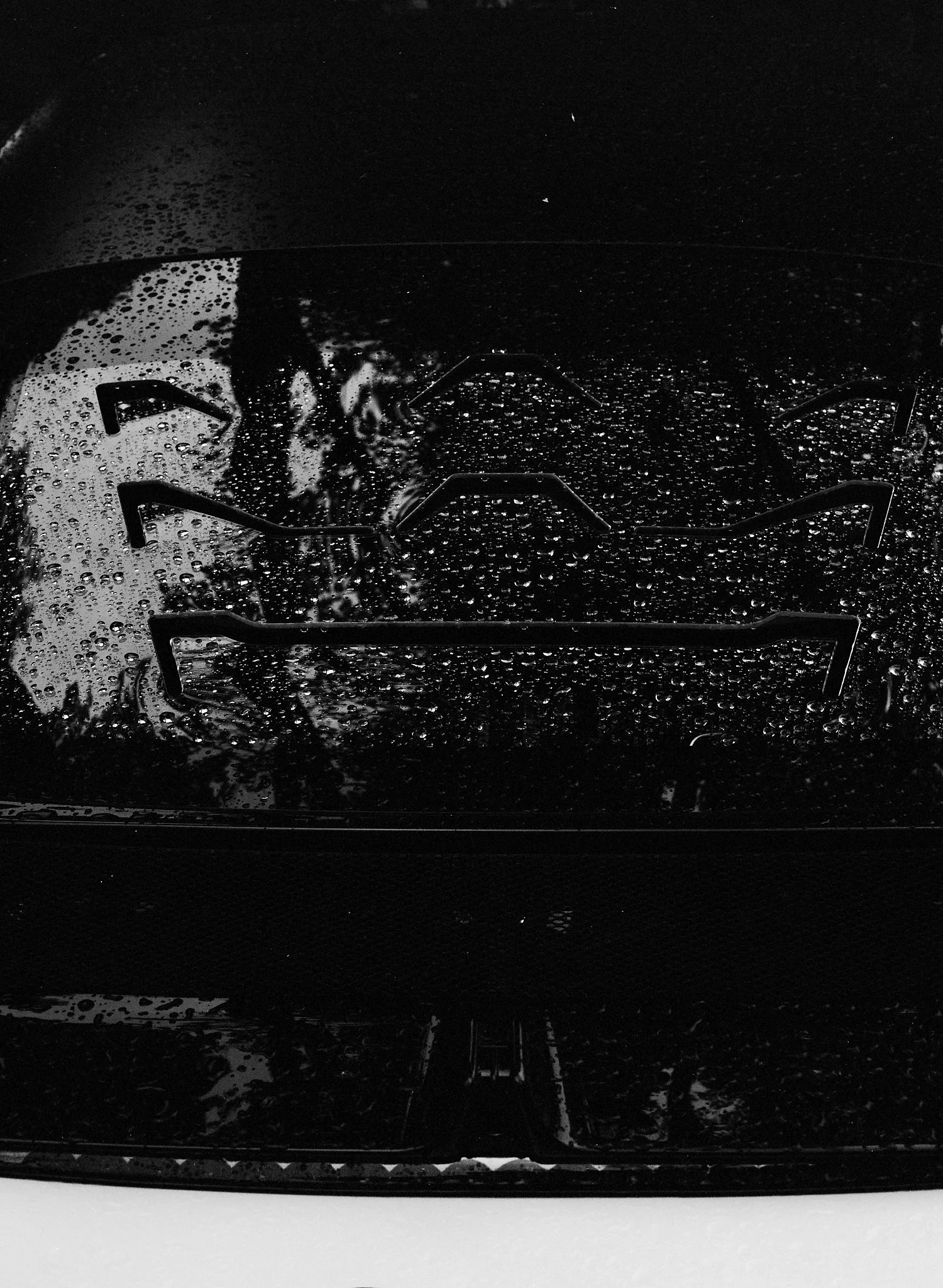 Close-up of a stove with water droplets on the black cooktop surface, reflecting a faint outline of a person and kitchen surroundings.