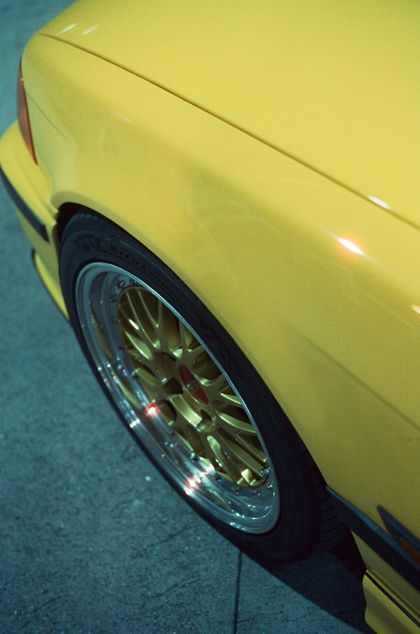Close-up of the side of a yellow sports car, showing the rear wheel with a gold-colored rim and the lower part of the car's body.