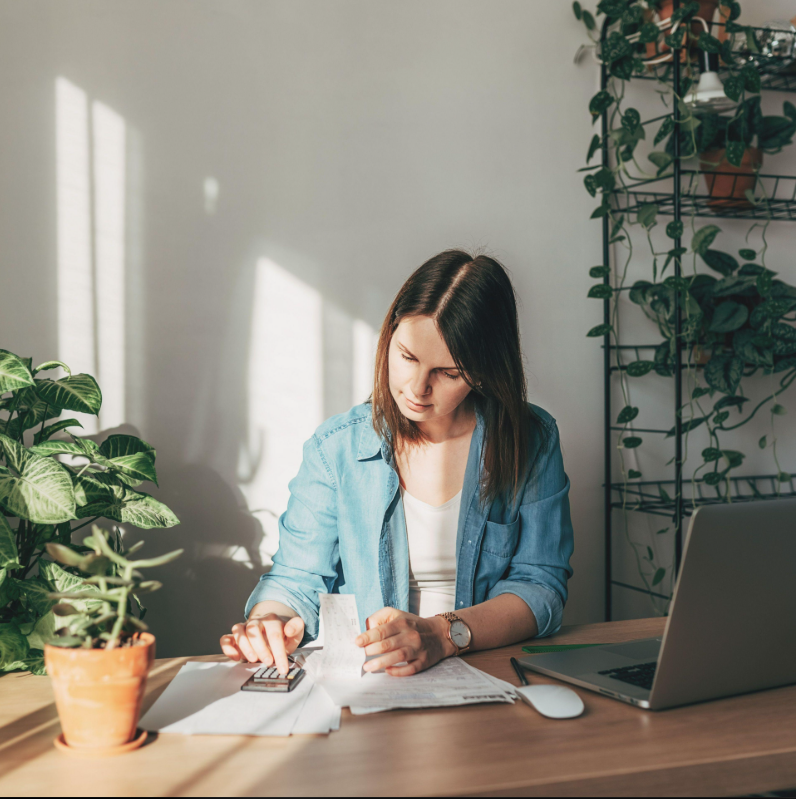 Bookkeeping workspace with a calculator, receipts, ledger, and laptop on a wooden desk.