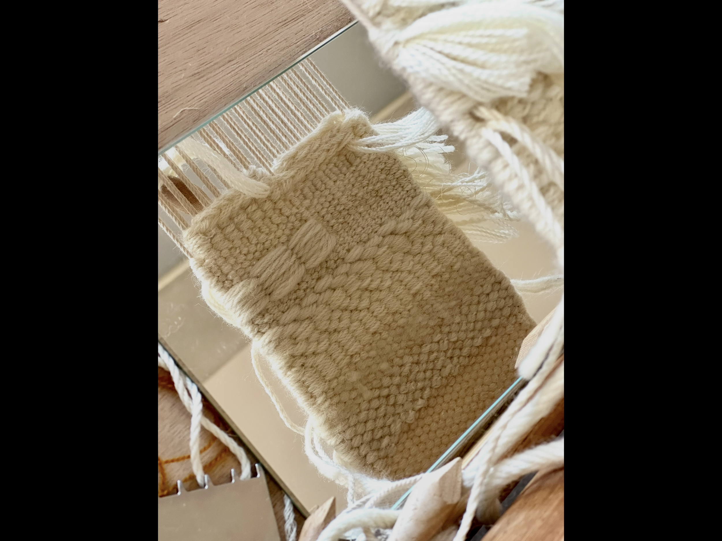 Une paire de chaussettes en laine beige posée sur un miroir. On peut voir une table en bois clair en dessous.